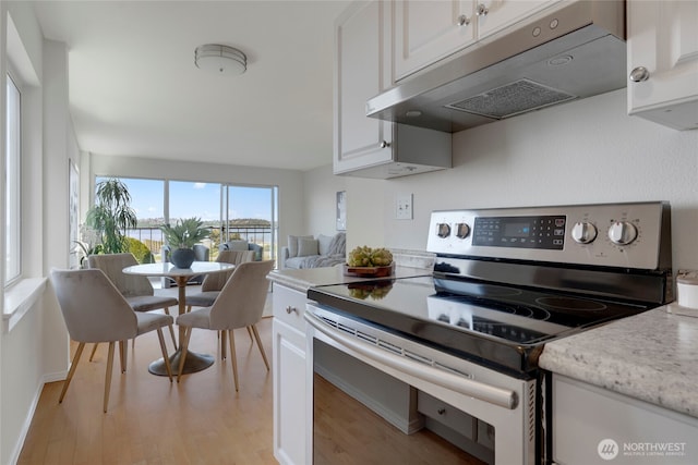 1156 Alki Ave SW Unit 105, Seattle, WA 98116 - kitchen with light stone countertops, light wood-style floors, under cabinet range hood, white cabinets, and stainless steel range with electric cooktop