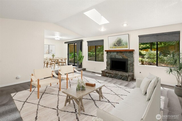 living room with vaulted ceiling with skylight, baseboards, a fireplace, and carpet flooring