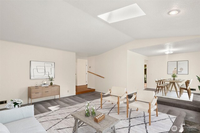 living area featuring baseboards, vaulted ceiling with skylight, and visible vents
