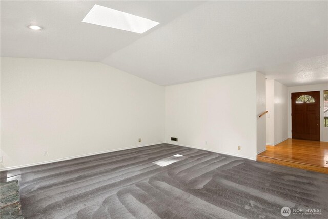 additional living space with baseboards, carpet flooring, wood finished floors, and vaulted ceiling with skylight