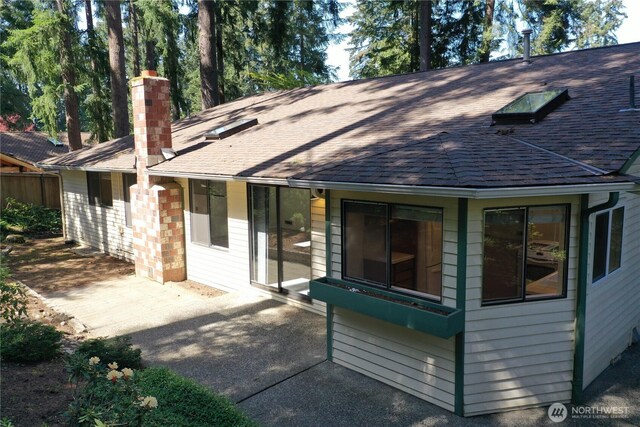 exterior space with a patio, a shingled roof, and a chimney