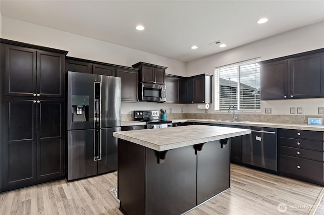 kitchen featuring a kitchen island, a kitchen bar, light countertops, a sink, and appliances with stainless steel finishes