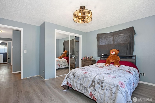 bedroom featuring an inviting chandelier, a textured ceiling, baseboards, wood finished floors, and a closet
