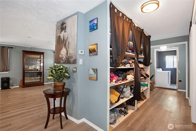 hallway featuring baseboards, a textured ceiling, wood finished floors, and washer / dryer