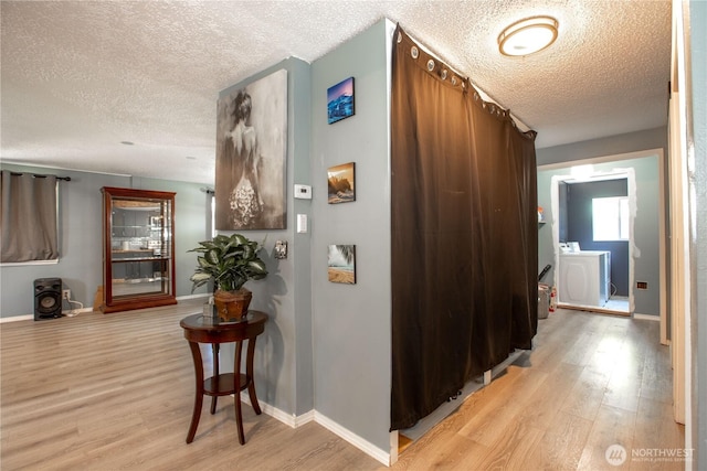 hall featuring baseboards, light wood-type flooring, and a textured ceiling