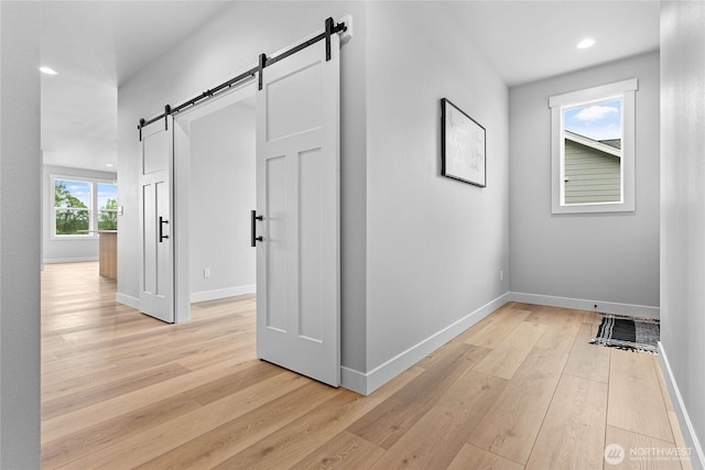 hallway with light wood-style floors, a barn door, baseboards, and recessed lighting