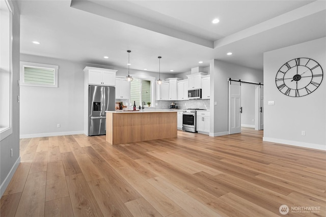 kitchen featuring recessed lighting, a barn door, white cabinetry, light wood-type flooring, and stainless steel appliances