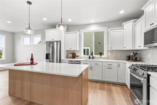 kitchen featuring white cabinets, appliances with stainless steel finishes, a sink, decorative backsplash, and a kitchen island
