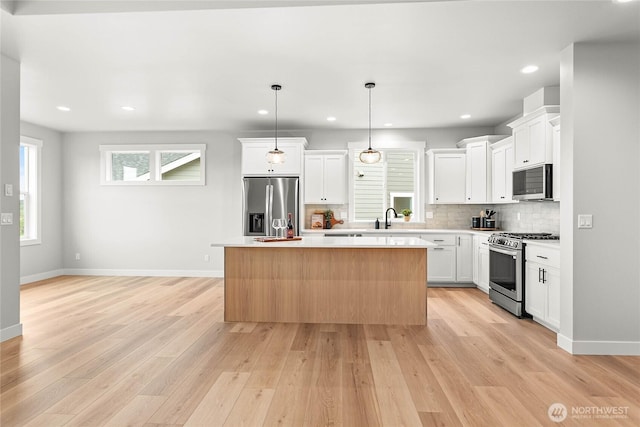 kitchen featuring appliances with stainless steel finishes, light countertops, a center island, baseboards, and backsplash