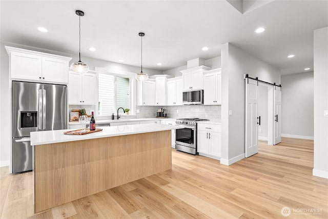 kitchen with a center island, a barn door, tasteful backsplash, light wood-style flooring, and appliances with stainless steel finishes