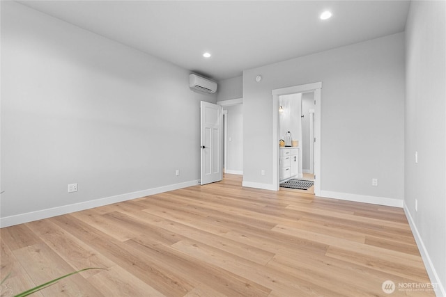 unfurnished bedroom featuring light wood-type flooring, a wall mounted air conditioner, baseboards, ensuite bathroom, and recessed lighting