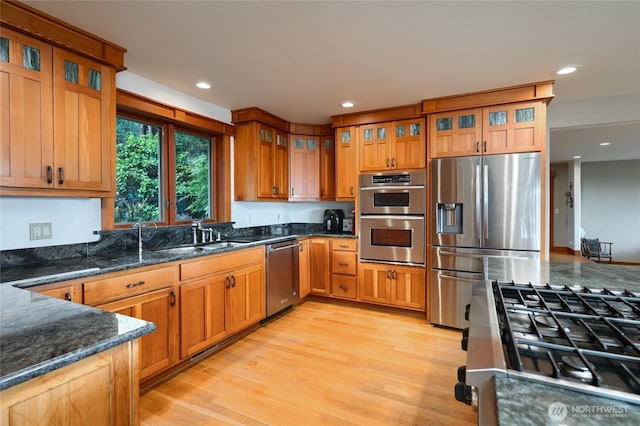 15089 Old Deception Mill Ln, Anacortes, WA 98221 - kitchen with glass insert cabinets, a sink, dark stone countertops, light wood-style floors, and stainless steel appliances