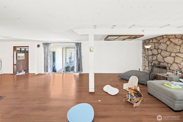 workout area featuring wood finished floors, a stone fireplace, and baseboards