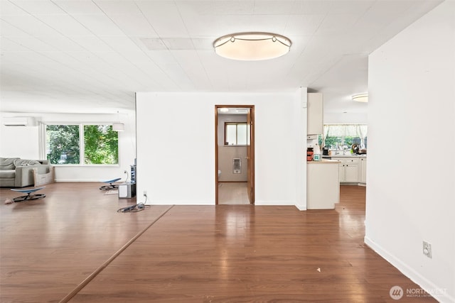unfurnished living room featuring an AC wall unit, plenty of natural light, and wood finished floors