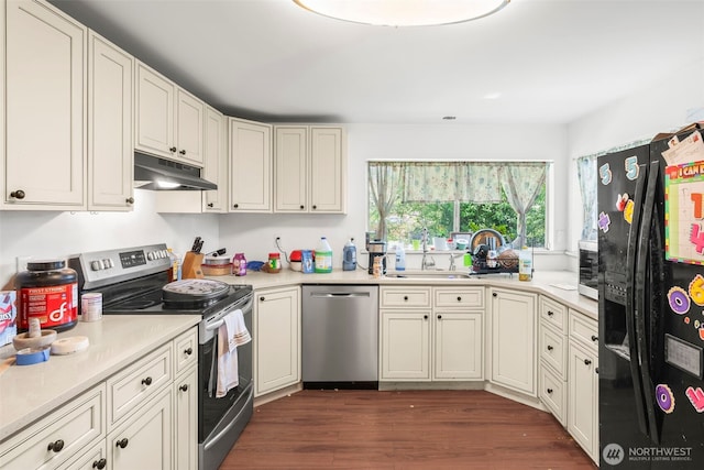 kitchen featuring appliances with stainless steel finishes, under cabinet range hood, dark wood finished floors, light countertops, and a sink