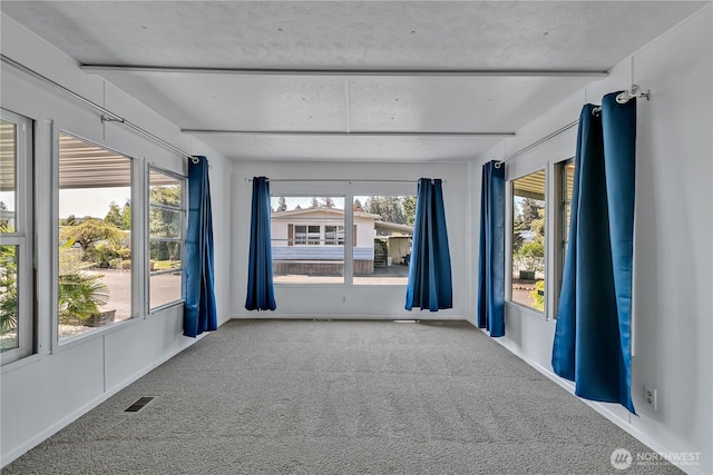 carpeted spare room featuring beamed ceiling, visible vents, and plenty of natural light