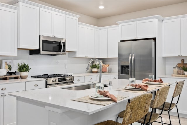 kitchen with a kitchen island with sink, a sink, stainless steel appliances, a breakfast bar, and white cabinetry