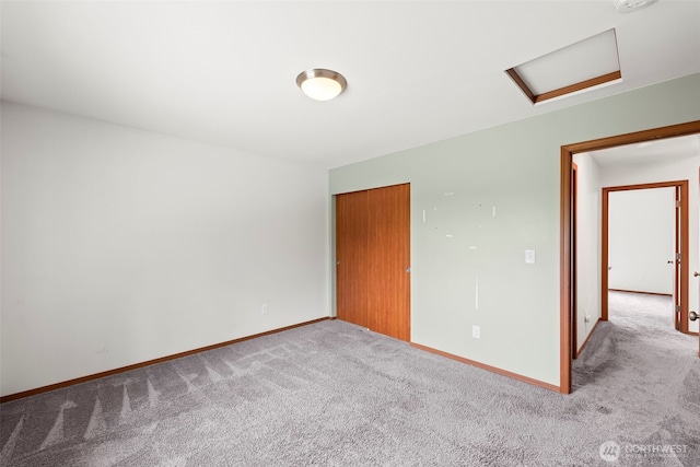 unfurnished room with baseboards, attic access, and carpet
