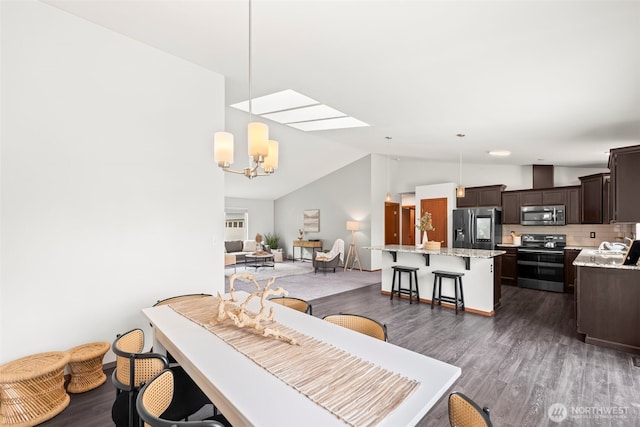 dining room with vaulted ceiling with skylight, dark wood-style flooring, and a chandelier