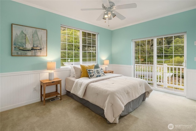 carpeted bedroom with crown molding, a ceiling fan, wainscoting, and access to exterior