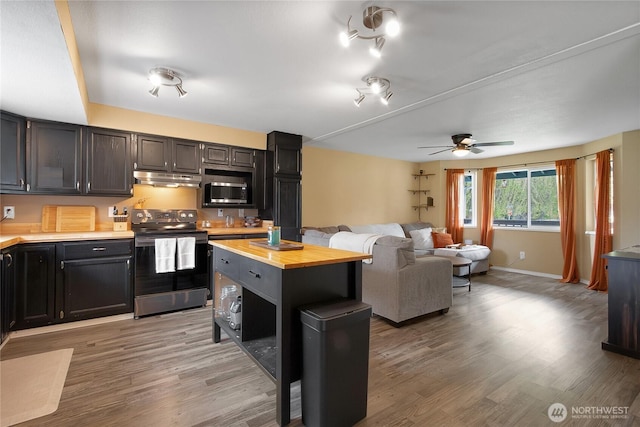 kitchen with butcher block countertops, electric range oven, stainless steel microwave, under cabinet range hood, and light wood-style flooring