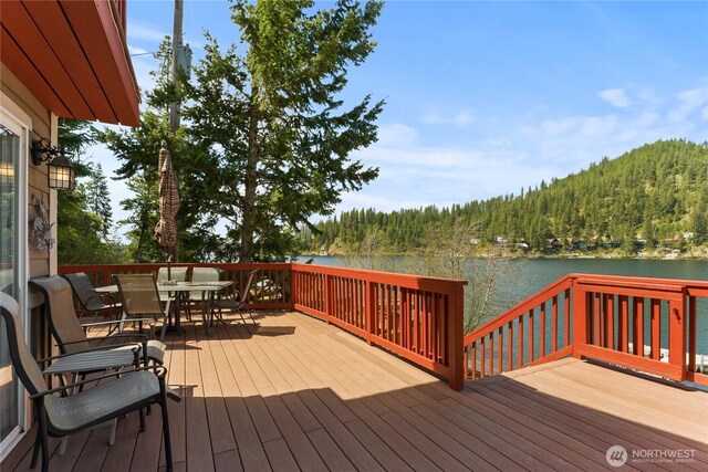 deck featuring outdoor dining space, a water view, and a wooded view