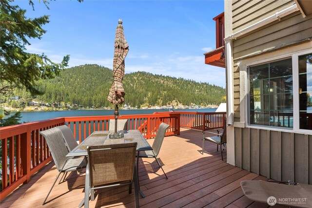deck with a water view, a view of trees, and outdoor dining area
