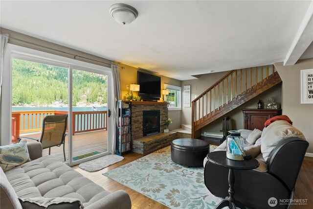 living room with baseboard heating, a fireplace, baseboards, wood finished floors, and stairway