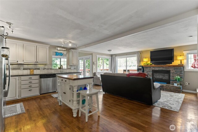 kitchen with dark countertops, dishwasher, white cabinets, open floor plan, and dark wood-type flooring