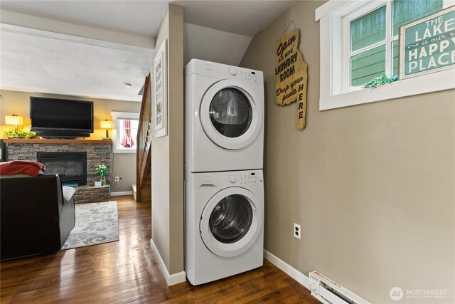 clothes washing area with baseboards, dark wood finished floors, stacked washer / dryer, and a fireplace