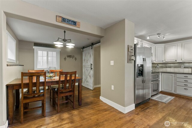 dining space featuring baseboards, a barn door, and wood finished floors