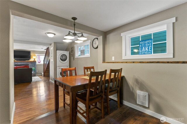 dining space with dark wood-style flooring, visible vents, a healthy amount of sunlight, and stacked washer / dryer