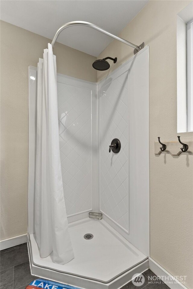 full bath with baseboards, tile patterned flooring, and a shower stall