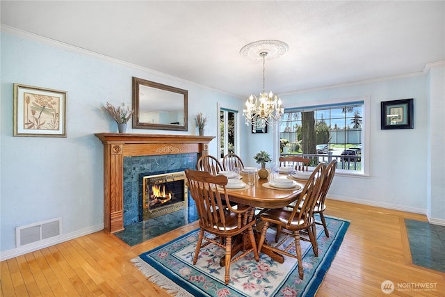 dining area with a chandelier, light wood-type flooring, a premium fireplace, crown molding, and baseboards