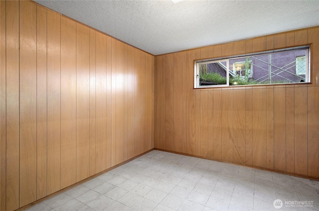 empty room featuring plenty of natural light, light floors, wood walls, and a textured ceiling