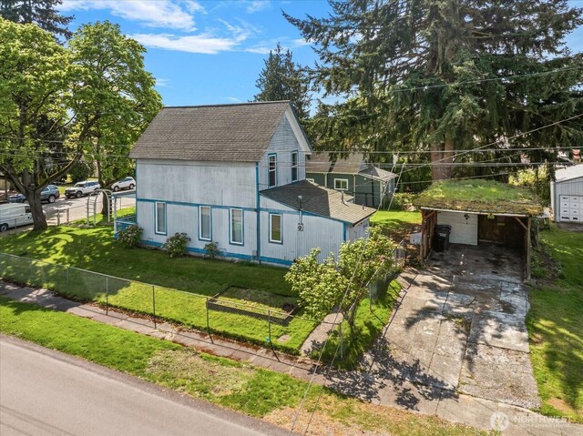 view of front of home with fence, driveway, a front yard, a shingled roof, and an outbuilding