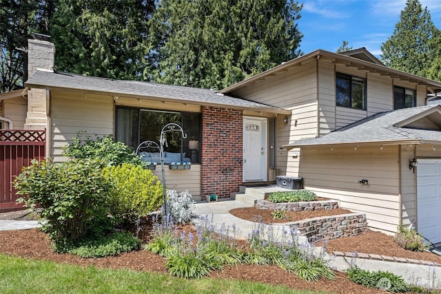 tri-level home with a chimney, roof with shingles, a garage, and fence