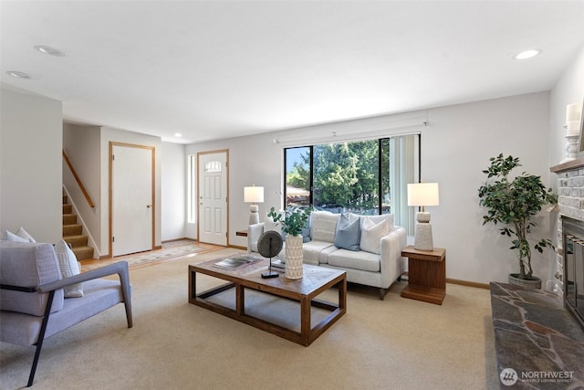 living area featuring a glass covered fireplace, stairway, light carpet, recessed lighting, and baseboards