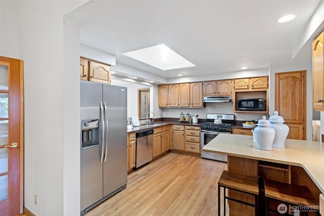 kitchen with stainless steel appliances, under cabinet range hood, a skylight, light brown cabinets, and a sink