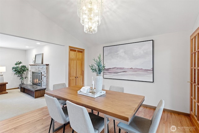 dining room featuring lofted ceiling, a brick fireplace, baseboards, a chandelier, and light wood-type flooring