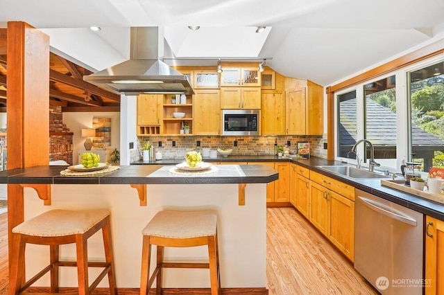 kitchen featuring appliances with stainless steel finishes, dark countertops, a sink, a breakfast bar, and light wood-style flooring