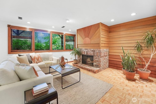 living area featuring wood walls, a brick fireplace, recessed lighting, and visible vents