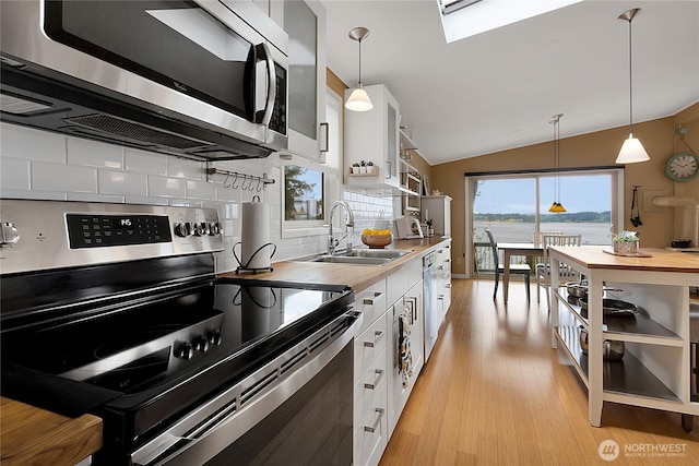 kitchen featuring a sink, light wood-style floors, stainless steel appliances, white cabinetry, and vaulted ceiling