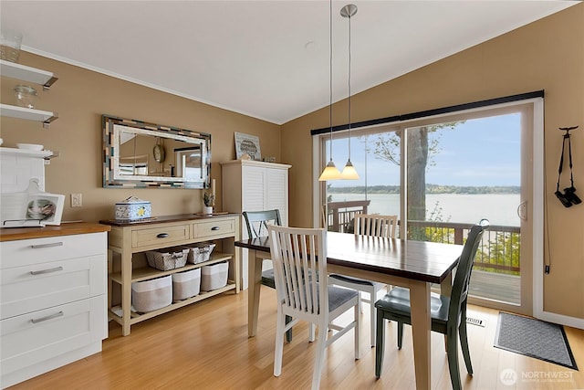 dining area with crown molding, a water view, vaulted ceiling, and light wood-type flooring