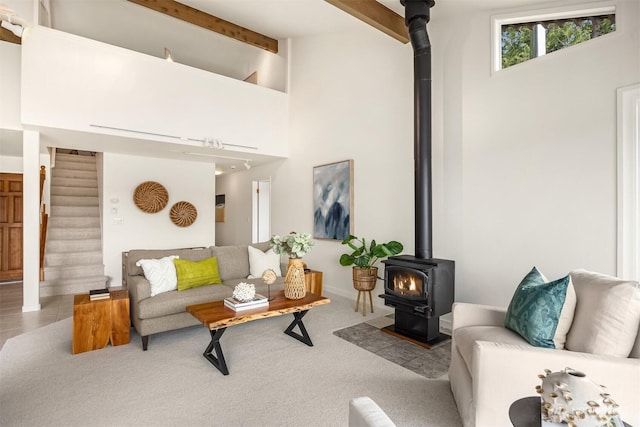 carpeted living area featuring beamed ceiling, stairway, and a wood stove
