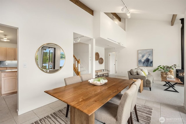 dining room featuring a wood stove, rail lighting, high vaulted ceiling, stairs, and light tile patterned flooring
