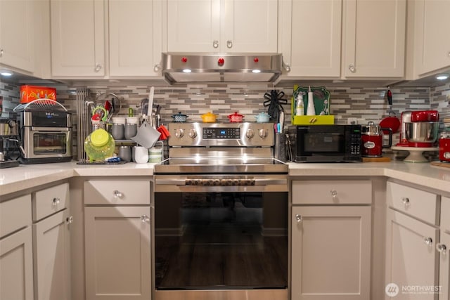 kitchen with stainless steel electric range, black microwave, light countertops, decorative backsplash, and range hood