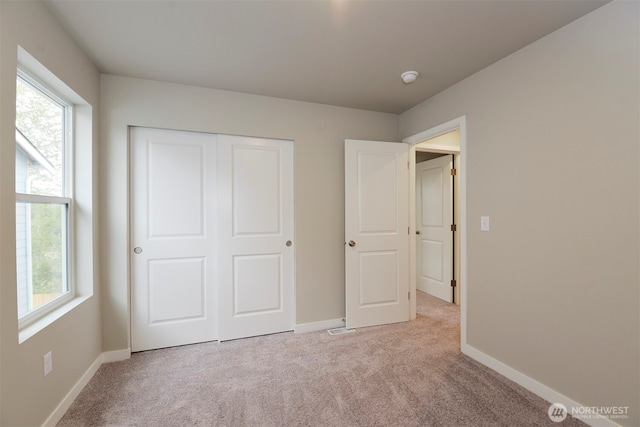 unfurnished bedroom with multiple windows, light carpet, and baseboards