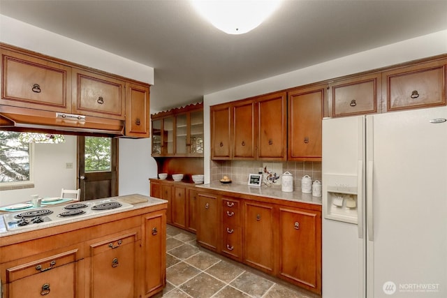 kitchen with white appliances, brown cabinets, backsplash, light countertops, and under cabinet range hood