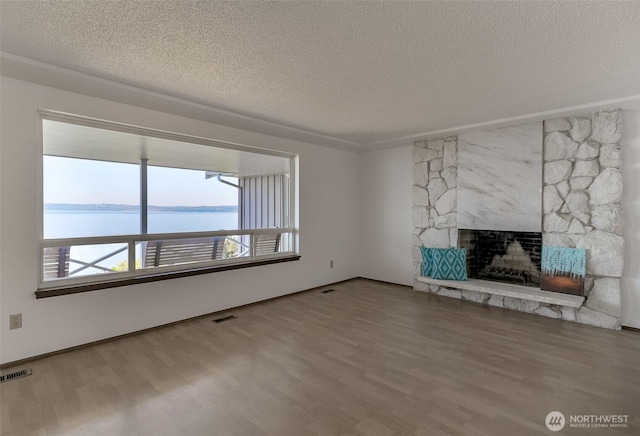 unfurnished living room with a textured ceiling, wood finished floors, a fireplace, and a water view